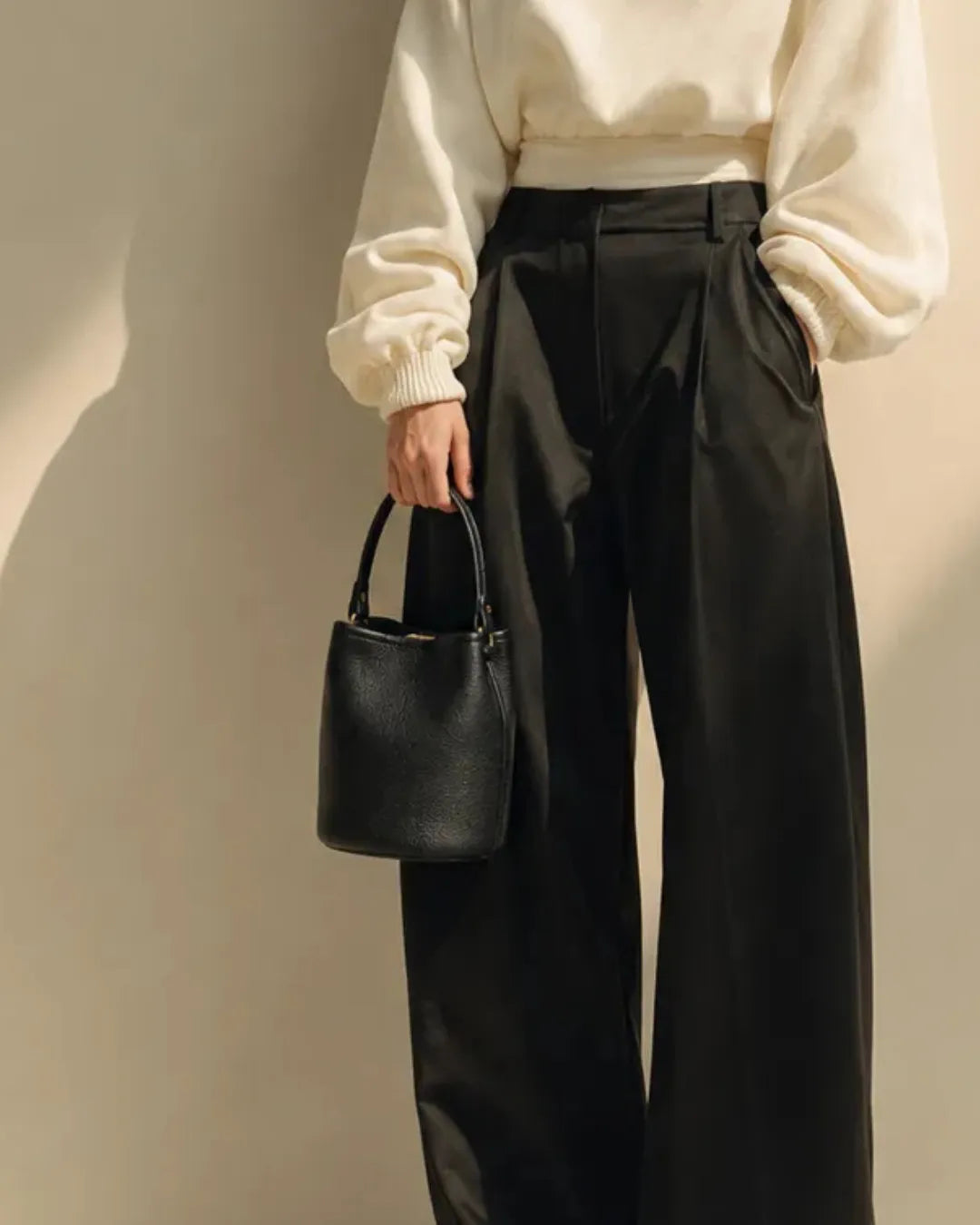 Model carrying The Bonnie genuine leather bucket bag by its top handle, highlighting the compact silhouette, premium pebbled leather and timeless minimalist design for everyday elegance.