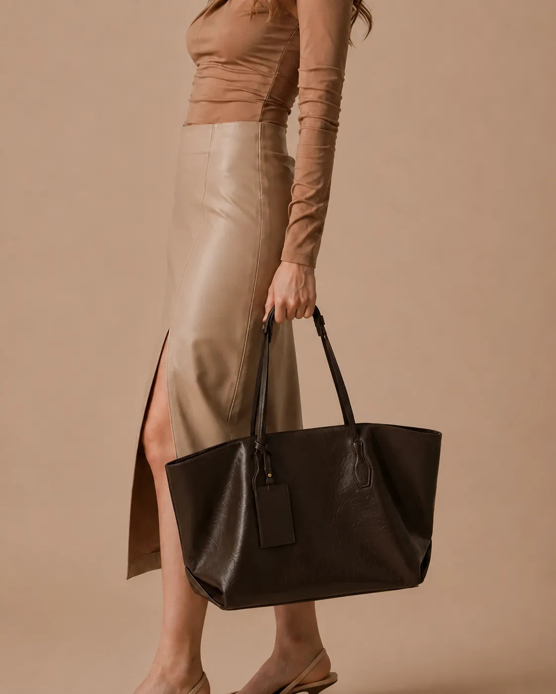 Model carrying The Emilia dark chocolate genuine leather tote bag by hand, showcasing its soft structured silhouette, spacious interior and elegant design for work, commuting and everyday use.