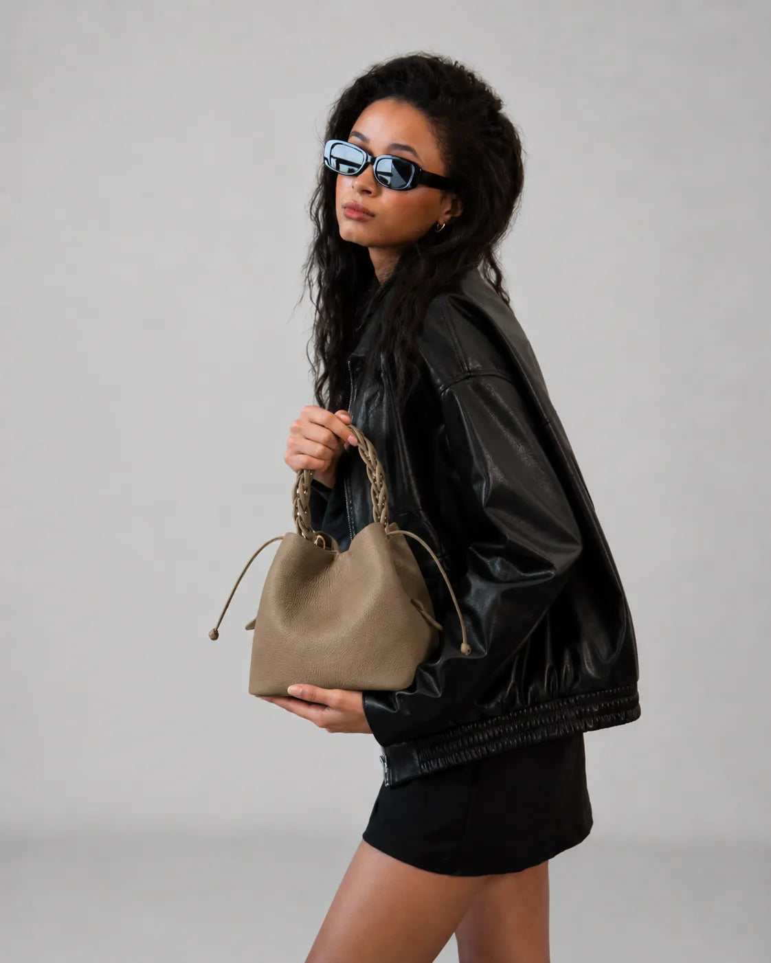Side view of model carrying The Léonie genuine leather bucket bag in Elephant Gray, premium women's leather handbag with braided top handles.