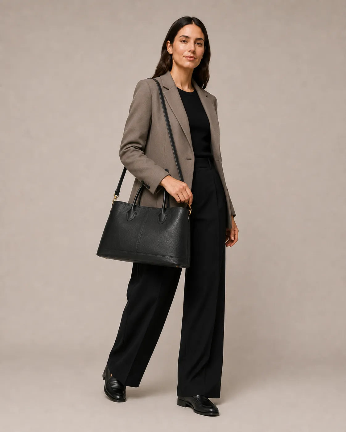 Woman holding the Odile large structured genuine leather tote bag in black by the top handles.