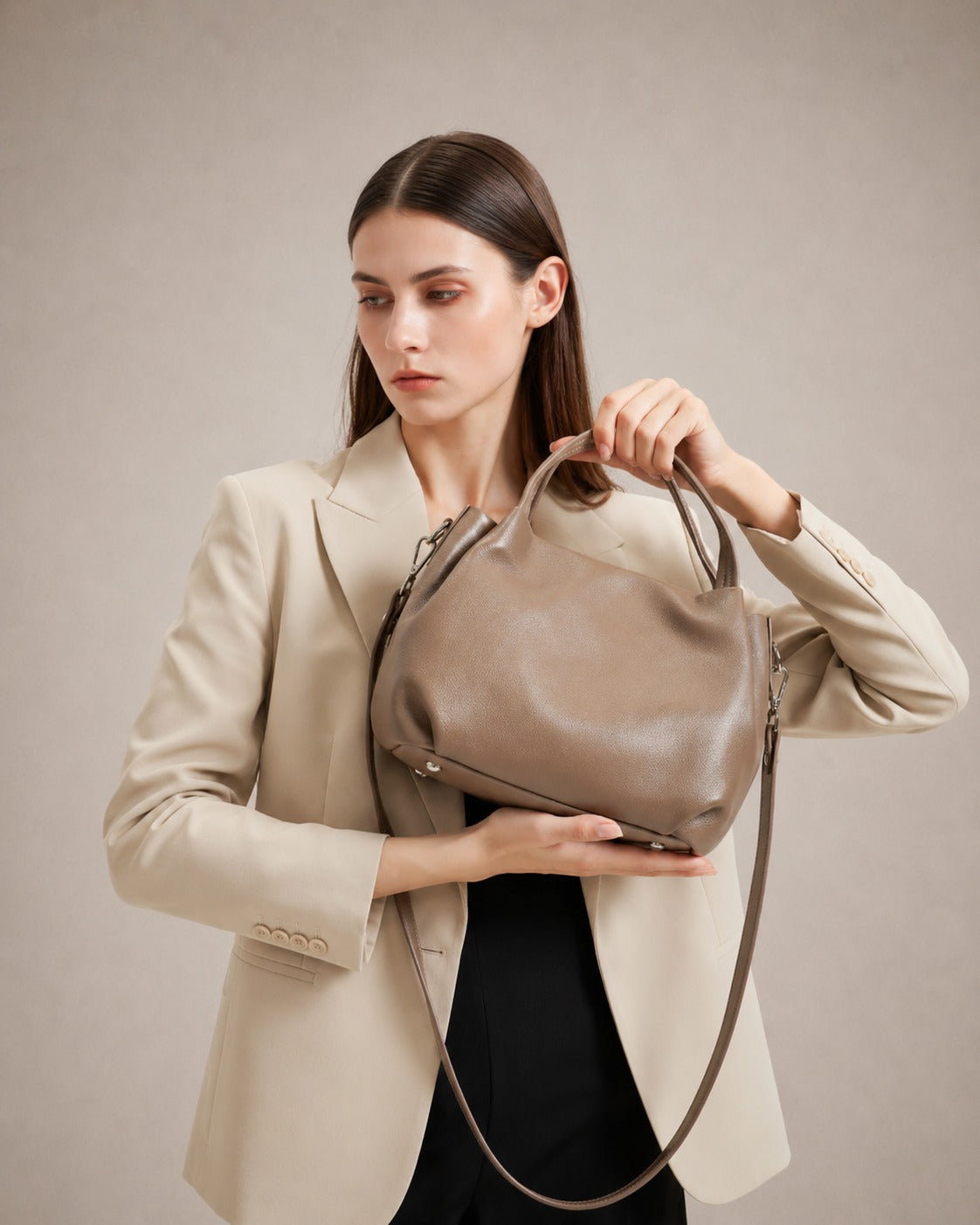Editorial lifestyle image of the Pauline genuine leather top handle crossbody bag in Taupe carried by a woman wearing a tailored blazer, highlighting timeless elegance and versatile everyday style by Malena London.