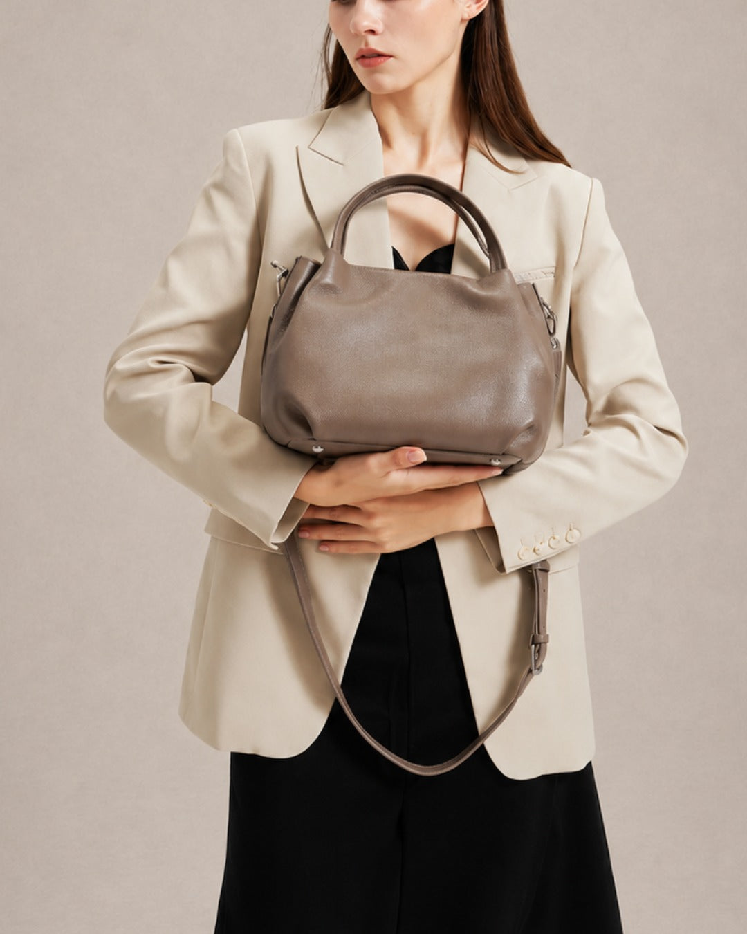 Woman holding the Pauline genuine leather top handle crossbody bag in Taupe, showcasing its elegant silhouette and refined day-to-evening styling by Malena London.
