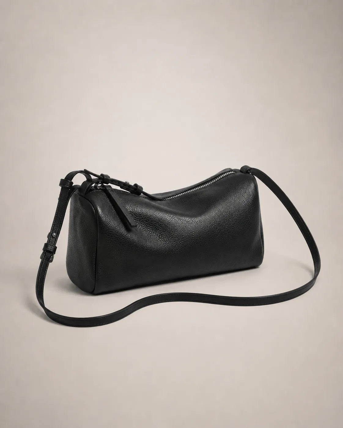 Angled view of the Simone genuine leather cylindrical crossbody bag in black showing the zip closure and adjustable strap.