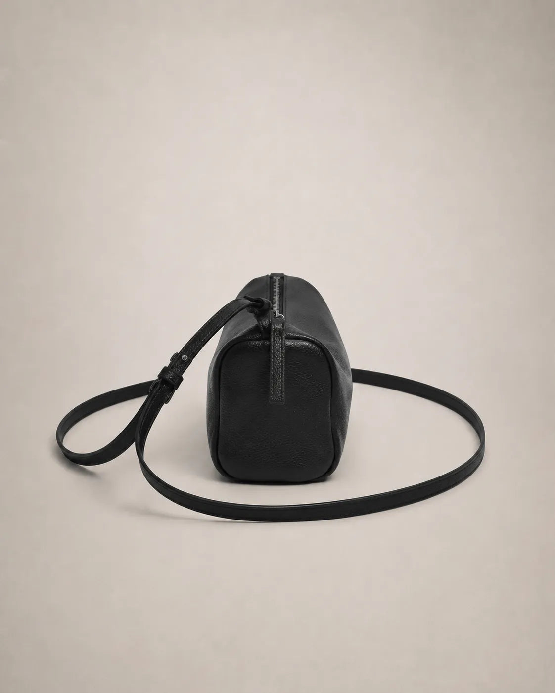 Back view of the Simone genuine leather cylindrical crossbody bag in black showing the end panel and coiled strap.