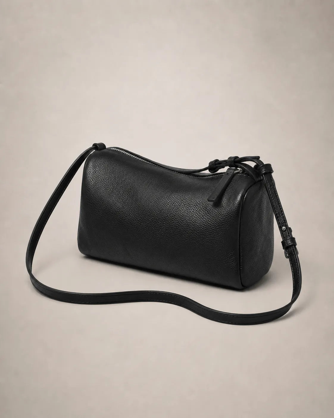 Three-quarter view of the Simone genuine leather cylindrical crossbody bag in black showing the cylindrical silhouette and strap.