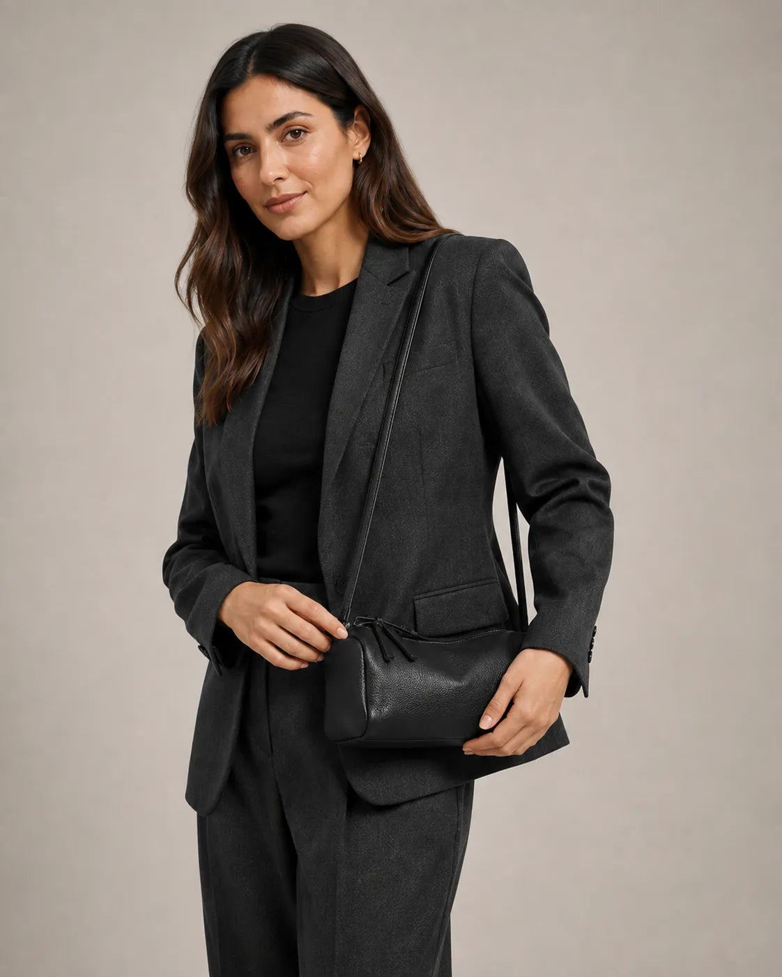 Woman wearing the Simone genuine leather cylindrical crossbody bag in black, held in hand with the strap worn across the body.