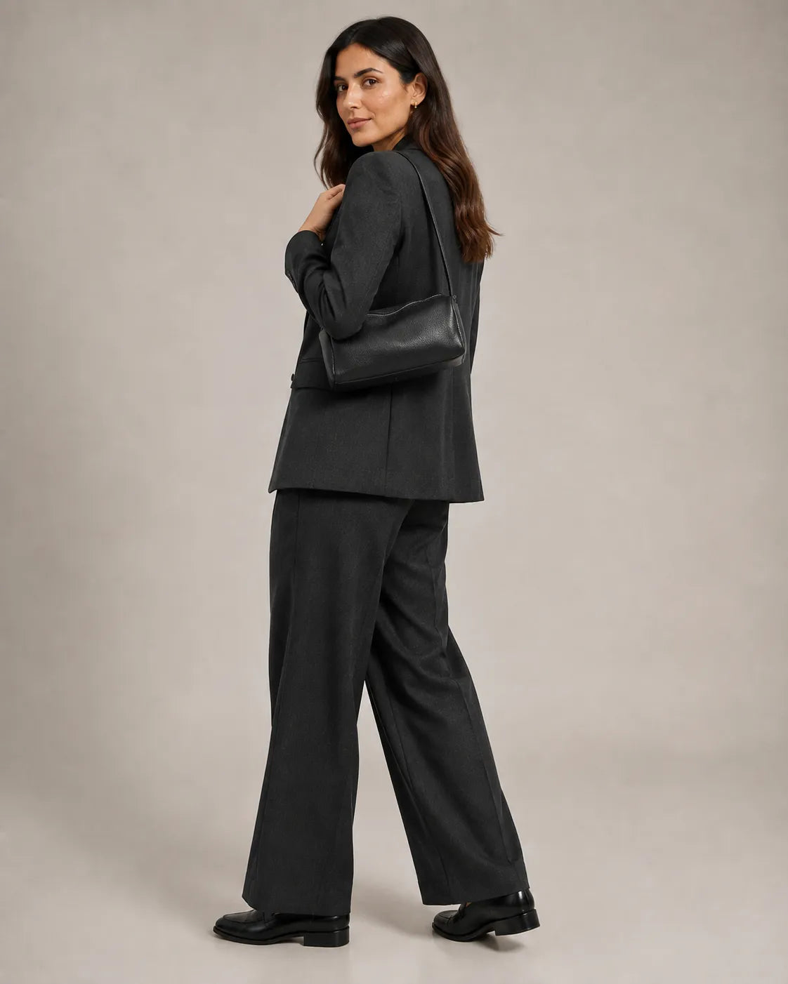 Woman wearing the Simone genuine leather cylindrical crossbody bag in black on the shoulder, back view.