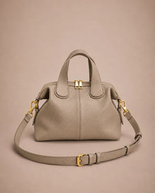 Victoire leather dumpling bag in Elephant Gray genuine leather featuring a soft structured silhouette, double top handles, adjustable shoulder strap, gold-tone hardware and zip closure, photographed from the front on the Malena London studio beige background.