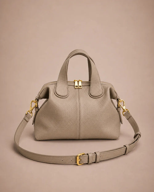 Victoire leather dumpling bag in Elephant Gray genuine leather featuring a soft structured silhouette, double top handles, adjustable shoulder strap, gold-tone hardware and zip closure, photographed from the front on the Malena London studio beige background.